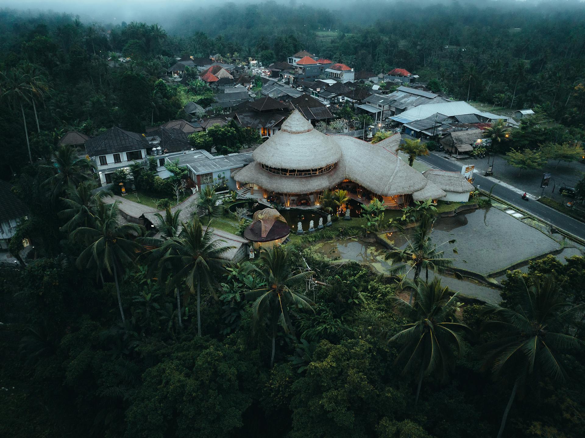 High-angle view of a hotel nestled in the Balinese jungle during a grey, misty monsoon storm.